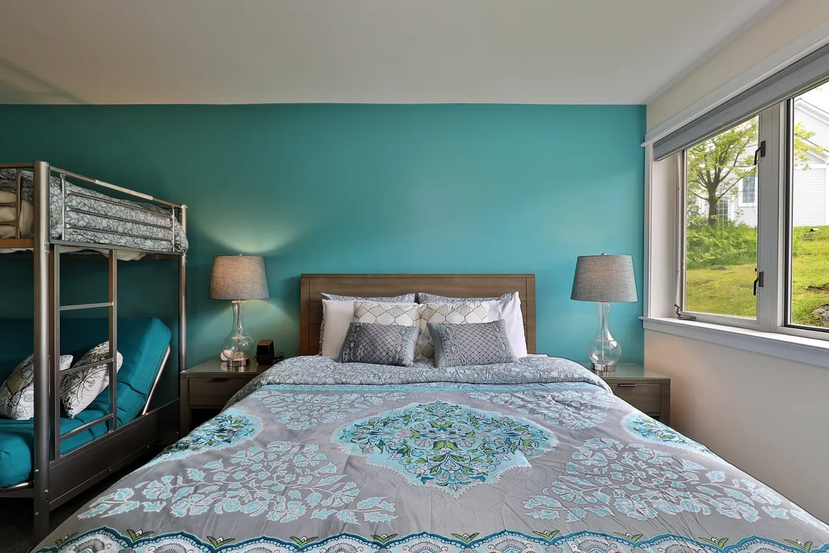 This photo captures another angle of the main studio, emphasizing the sleeping arrangements: a main bed with decorative bedding, a playful bunk bed, soft table lamps, and a window letting natural light stream in. The room feels open and welcoming, perfect for group relaxation or quiet morning routines.